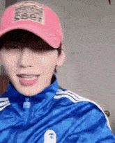 a young man wearing a pink hat and a blue jacket is making a funny face .