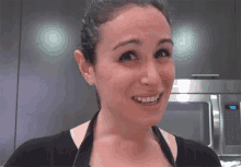 a woman wearing an apron is smiling in front of a microwave that has the time of 9:38