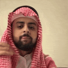 a man with a beard is wearing a red and white keffiyeh and headphones .