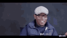 a man wearing glasses and a flat cap is laughing