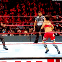 a female wrestler in a red top and blue pants is in a wrestling ring