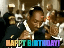 snoop dogg is wearing a suit and tie and holding a microphone and says happy birthday .