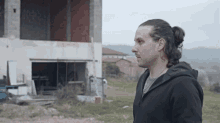 a man with long hair in a ponytail stands in front of a building