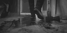 a black and white photo of a person holding a bloody axe on the floor .