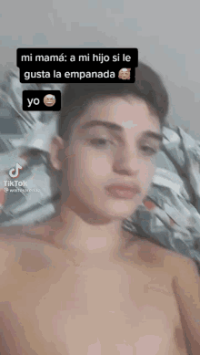 a young man without a shirt is laying on a bed and has a tiktok app on his phone