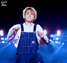 a man wearing overalls and a white shirt is singing into a microphone with the word promise on the bottom right