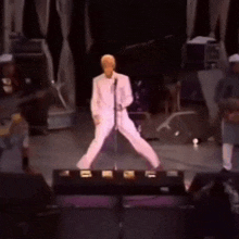 a man in a white suit sings into a microphone on a stage
