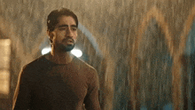 a man is standing in the rain at night and looking at the camera .