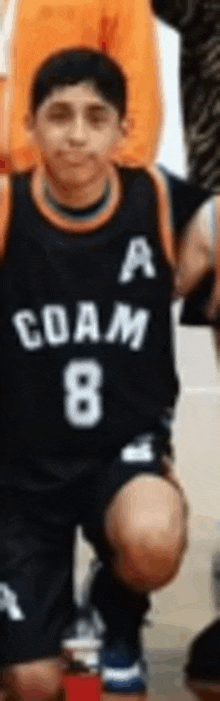 a young boy wearing a black jersey with the number 8 on it is kneeling down on a basketball court .