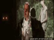a man with blood on his face is running in a dark room with a woman behind him .