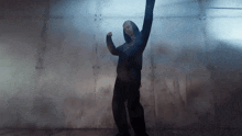 a man in a blue hoodie is dancing in front of a wall
