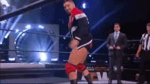 a man in a suit and tie is standing in a wrestling ring while a referee watches .