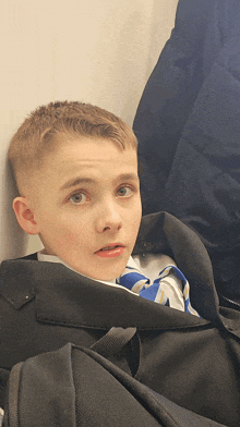 a young boy sitting in a black bag with a blue and white shirt on