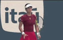 a woman wearing a red shirt and a white visor stands in front of a sign that says " jitsu "