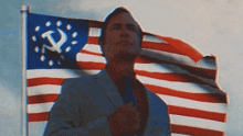 a man in a suit stands in front of an american flag