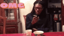 a man is sitting at a table with a cup of coffee and looking at his cell phone .