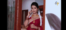 a woman in a red and gold saree is talking on a cell phone