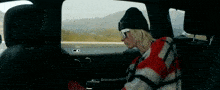 a woman is sitting in the back seat of a car wearing a hat and goggles .