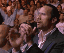 a man in a suit is sitting in front of a crowd applauding .