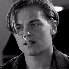a close up of a man smoking a cigarette in a black and white photo .