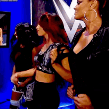 three women are standing next to each other in front of a w logo on a wall