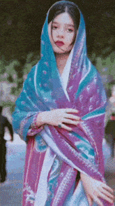 a woman wearing a blue and purple scarf is standing in front of a green background .