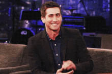 a man in a suit is sitting on a couch with his hands in his pockets