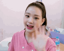 a girl in a pink shirt is waving her hand in front of a bottle of aquafina water