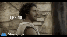 a man with curly hair is standing in front of a stone wall with the words lurking written on the bottom