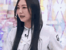 a woman with long black hair is wearing a white jacket and a microphone .