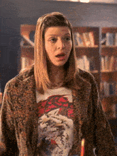 a woman wearing a leopard print jacket and a t-shirt with a dragon on it stands in front of a bookshelf