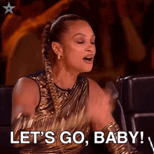 a woman in a gold dress says let 's go baby in front of a microphone