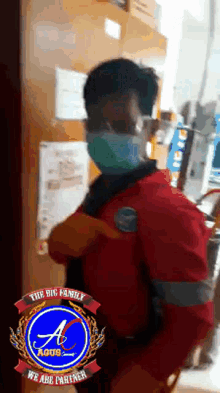 a man wearing a red shirt and a mask stands in front of a sign that says " the big family "