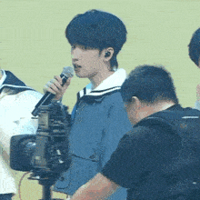 a young man is singing into a microphone while another man looks on