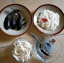 a table topped with bowls of food , including rice , fish , noodles , and a spoon .