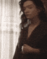 a woman is standing in front of a window wearing a black jacket and a plunging neckline .