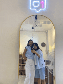 two women taking a picture in front of a mirror that says dr selfshoot studio