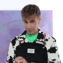 a young man wearing a cow print jacket and an apron is standing in front of a painting .