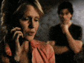 a woman is talking on a cell phone with a man behind her
