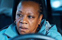 a woman in a blue jacket and hoop earrings is driving a car