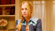 a woman in a blue cowboy jacket is standing in a room with plates on the shelves .