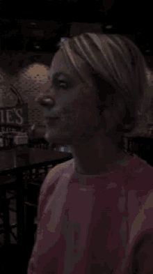 a woman in a pink sweater is smiling in front of a sign that says nie 's