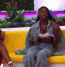 a woman in a denim jacket is sitting on a yellow couch holding a drink .
