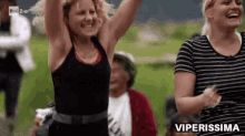 a woman in a black tank top is dancing with her arms in the air in front of a crowd of people .