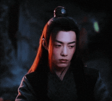 a man with long red hair and a ponytail looks at the camera