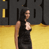 a woman in a black dress stands on a yellow carpet in front of a sign that says hbo