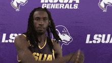 a man wearing a lsua jersey stands in front of a purple banner