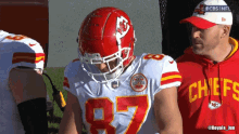 a man wearing a chiefs sweatshirt talks to a player