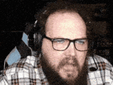 a man with a beard and glasses is wearing headphones and a plaid shirt .