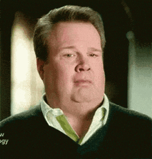 a man with a double chin is making a funny face while wearing a black sweater and a white shirt .